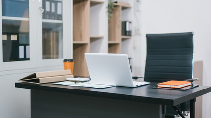 A modern office workspace with a black desk, documents, a coffee cup, and a laptop. The empty ergonomic chair and neat setup reflect professionalism, organization, and corporate productivity