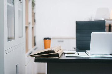 A modern office workspace with a black desk, documents, a coffee cup, and a laptop. The empty ergonomic chair and neat setup reflect professionalism, organization, and corporate productivity