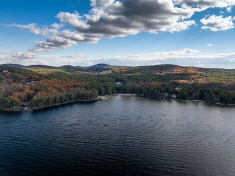 Aerial view of the tranquil lake mirroring the clear sky, bordered by vibrant autumn foliage and rolling hills, Alton, New Hampshire, United States.