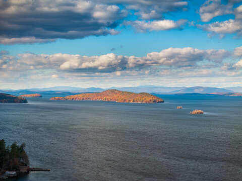 Aerial view of autumn foliage ablaze on islands dotting the expansive lake under a vast sky of scattered clouds, Alton, New Hampshire, United States.