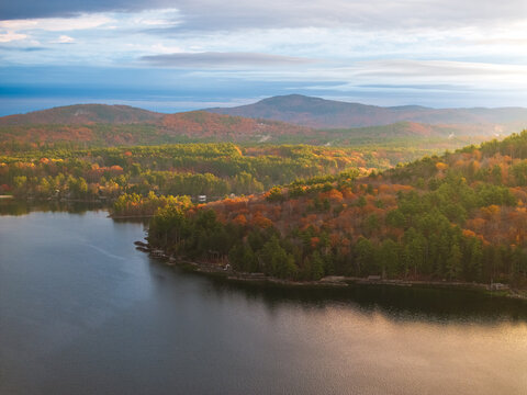 Aerial view of the sun kissing the tranquil waters as autumn's vibrant hues paint the landscape near Alton Bay, Alton, New Hampshire, United States.