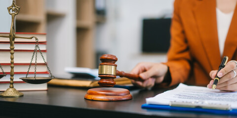 A young Asian woman in a formal blazer works confidently on her laptop in a modern office, surrounded by legal documents and professional tools, reflecting expertise, focus, and a polished corporate