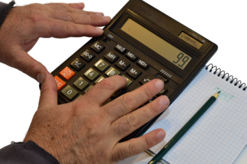 A man is working on a calculator, with a notepad and pencil lying nearby.