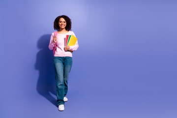 Young female student smiles carrying notebooks pink backpack against violet background casual fashion school lifestyle education youth advertising
