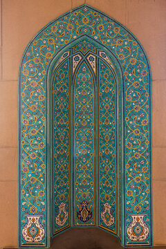 View of intricately patterned teal and gold archway beckons with detailed floral motifs against a smooth, warm stone wall, Muscat, Muscat Governorate, Oman.