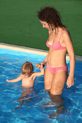 A woman is holding a child in a pool. The woman is wearing a pink bikini. The child is in the water...