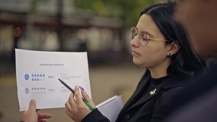 A young businesswoman passionately explains a finance info graphic to her colleague. They discuss financial data and strategies, highlighting collaboration and business analytics in an urban setting. - Powered by Adobe