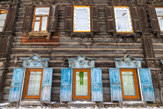 View of weathered wooden facade adorned with intricately carved window frames and vibrant blue shutters, creating a striking contrast against the aged wood, Irkutsk, Irkutsk Oblast, Russia.