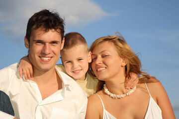 Fototapeta premium A man, a woman and a child are smiling and posing for a picture. The man is wearing a white shirt and the woman is wearing a white dress. Scene is happy and joyful