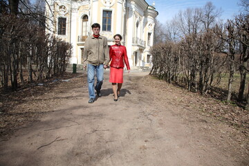 Obraz premium A man and woman are walking down a path in front of a large building. The man is wearing a jacket and jeans, while the woman is wearing a red dress. Scene is romantic and peaceful