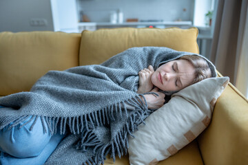Exhausted woman lying on sofa shivering under blanket. Emotional fatigue, mental health problems, deep social isolation, depression. Sick unwell female with cold, flu symptom suffer chills, malaise.