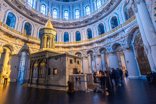 View of a grand interior with intricate white and gold detailing, a central structure, and people gathered, bathed in soft light, Istra, Moskovskaya oblast', Russia.