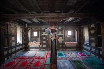View of prayer rugs scattered across the floor, light streaming through arched windows in a room with wooden beams and pillar, Shigar, Gilgit Baltistan, Pakistan.