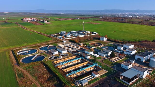 Approaching the territory of modern wastewater treatment plant. Diverse reservoirs are filled with sewage water. Green fields are around the facility.