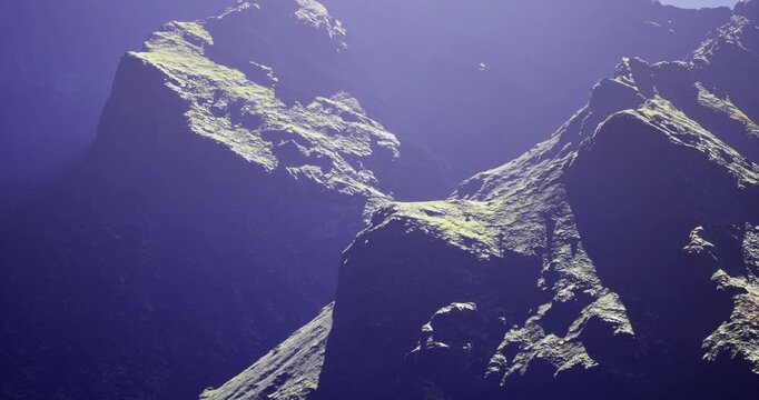 A striking mountain range showcases rugged peaks illuminated by bright sunlight. The high terrain features rocky surfaces with patches of green vegetation, highlighting natures grandeur.