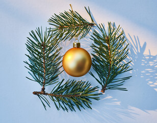 Golden Christmas Ornament Hanging on Lush Green Pine Branches Against a Clean White Background in Minimalist Holiday Still Life Photography
