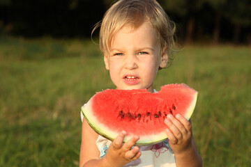 A young girl is holding a watermelon slice in her hand. She looks surprised and is about to take a bite