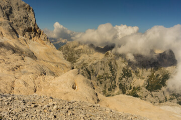 View of jagged peaks and rocky terrain meet ethereal clouds under a blue sky, creating a breathtaking alpine vista, Triglavski narodni park, Gorenjska, Slovenia.