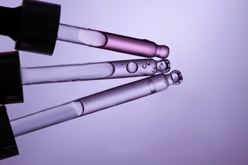 Fototapeta premium Three glass pipettes with facial serum on light purple background. Front view. Frontal close-up view of liquid gel/essential oil, banner for advertising anti-aging cosmetic product with bakuchiol, spi