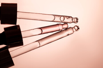 Three glass pipettes with facial serum on light orange background. Front view. Frontal close-up view of liquid gel/essential oil, banner for advertising anti-aging cosmetic product with bakuchiol, spi
