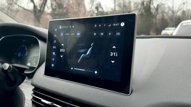 In-car footage shows a hand interacting with a large, modern infotainment touchscreen displaying the digital climate control system.
