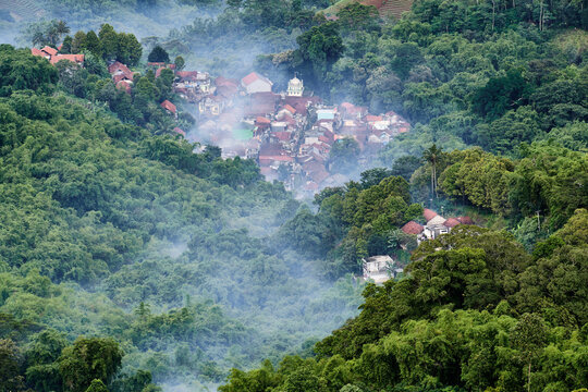 View of a village nestled among dense green trees, shrouded in mist, in Panyaweuyan, Majalengka, West Java, Indonesia.