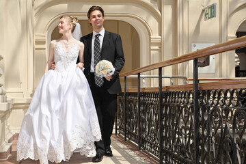 A bride and groom are walking down a staircase, the bride holding a bouquet. Concept of love and...