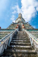 Detailed view of the ornate towers of Wat Arun in Bangkok, Thailand, showcasing rich ceramic floral patterns, sculpted figures, and intricate decorations under bright daylight.