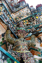 Detailed view of the ornate towers of Wat Arun in Bangkok, Thailand, showcasing rich ceramic floral patterns, sculpted figures, and intricate decorations under bright daylight.