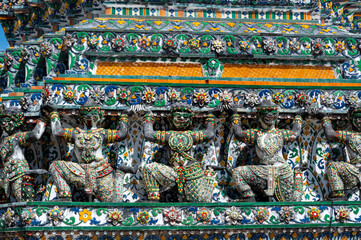 Detailed view of the ornate towers of Wat Arun in Bangkok, Thailand, showcasing rich ceramic floral patterns, sculpted figures, and intricate decorations under bright daylight.