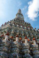 Detailed view of the ornate towers of Wat Arun in Bangkok, Thailand, showcasing rich ceramic floral patterns, sculpted figures, and intricate decorations under bright daylight.