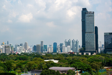 Panoramic view of Bangkok distant high-rise buildings with Lumphini Park in the foreground, combining calm green spaces and a broad city skyline under bright daylight.
