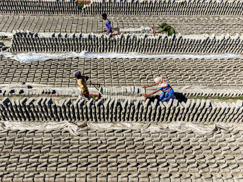 Narayanganj, Bangladesh - 09 November 2024: Aerial view of workers amidst the brickfields, their figures small against the vast expanse of drying bricks, a tapestry of earthy tones under the open sky.