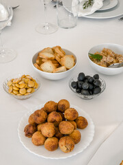 A table is set with a selection of savory appetizers for guests, including meat croquettes, sliced stuffed bread, black olives, crisp toast, lupin beans and pate, ready to share before a festive meal