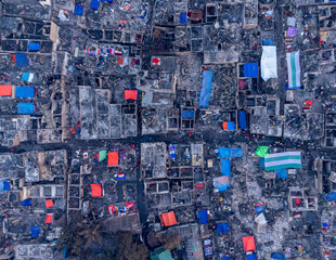 Dhaka, Bangladesh - 28 November 2025: Aerial view of a densely packed urban area with a stark contrast between the dark rooftops and vibrant tarpaulins spread across the structures.