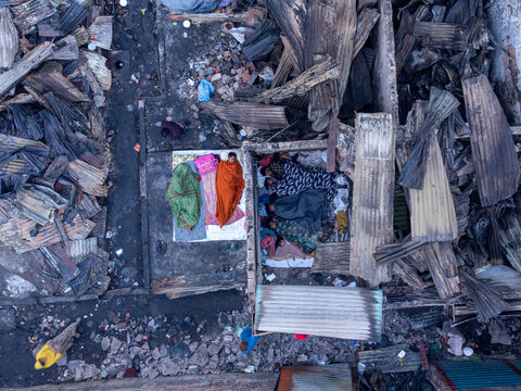 Dhaka, Bangladesh - 28 November 2025: Aerial view of a slum where the harsh aftermath of a fire is evident, with charred debris surrounding people sleeping on makeshift beds.