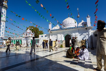 Bhit Shah, Pakistan - 05 December 2025: View of the bustling courtyard of the Shrine of Abdul Shah, where pilgrims in vibrant clothing gather under a canopy of festive flags.