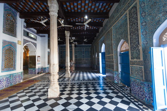 Bhit Shah, Pakistan - 05 December 2025: View of the interior hall with checkered floors, ornate blue and white tiled walls, and tall white pillars supporting a dark wooden ceiling.