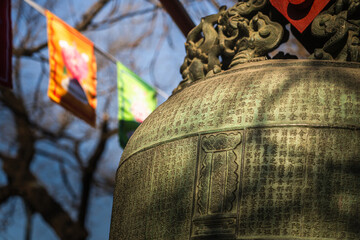 Beijing, China - 26 November 2025: View of an ancient bronze bell adorned with intricate carvings stands in stark contrast to the vibrant flags.
