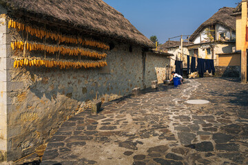 Honghe Hani and Yi Autonomous Prefecture, China - 21 November 2025: View of traditional stone houses with thatched roofs, corn cobs drying, and clothes hanging in the village street.