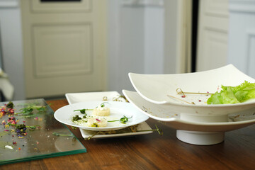 Dirty dishes with food remnants and scattered ingredients on a wooden table after a banquet, showcasing the aftermath of a festive dining experience