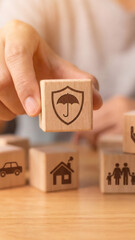 A hand holds a wooden block with an insurance protection icon. Concept of coverage for family, home, and car. Financial planning and risk management