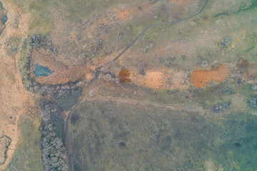 Top down view of winding dirt road crossing swampy fields with dry reeds and green grass, high quality aerial drone shot of rural wilderness nature texture