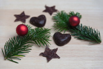 Gingerbread hearts with Christmas tree balls, fir branches, stars on wooden surface with blurred background