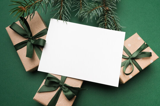 Christmas greeting card mockup with blank space surrounded by wrapped gifts and evergreen branches, perfect for holiday wishes and seasonal greetings