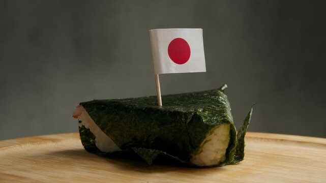 Close up shot of single onigiri wrapped in nori with Japanese flag on toothpick, scene highlights traditional Japanese rice, local seaweed and classic convenience food culture.