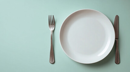 Minimalist dining setting with white plate, fork, and knife on a light teal background, copy space