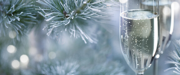 Two filled champagne glasses outdoors in front of frozen pine branches with hellen bokeh lights....