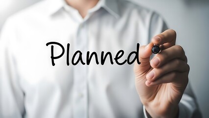 Businessman writing the word planned in cursive script on a transparent surface with a marker pen