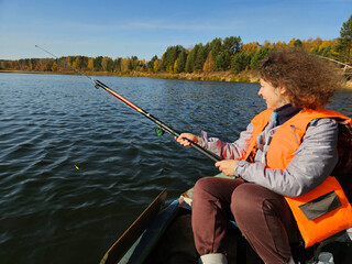 Fototapeta premium Woman in an orange life jacket is fishing in a boat. She is holding a fishing pole and has a fish on it